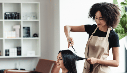 A stylist works on her client's hair as she ponders beauty insurance.