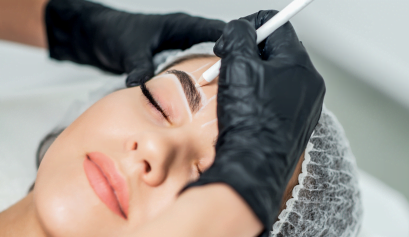 A customer sits back and relaxes as she gets her eyebrows microbladed by a trained beauty pro.