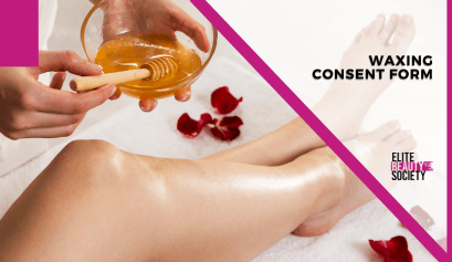 A close-up of a person’s smooth, bare leg resting on a soft white towel with scattered red rose petals. A hand is holding a bowl of golden honey-like wax with a wooden applicator, preparing to apply the wax for a hair removal treatment.